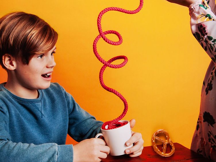 Junge hält Tasse in der Hand und es fällt eine Kordel in die Tasse