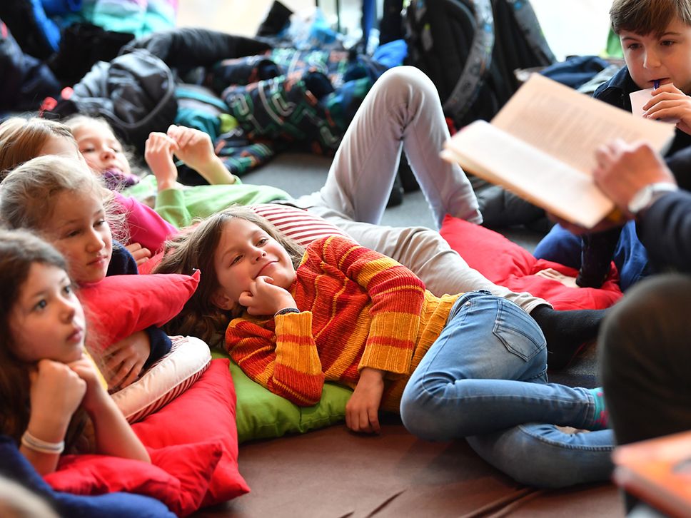 Kinder liegen auf dem Boden und hören beim Vorlesen zu