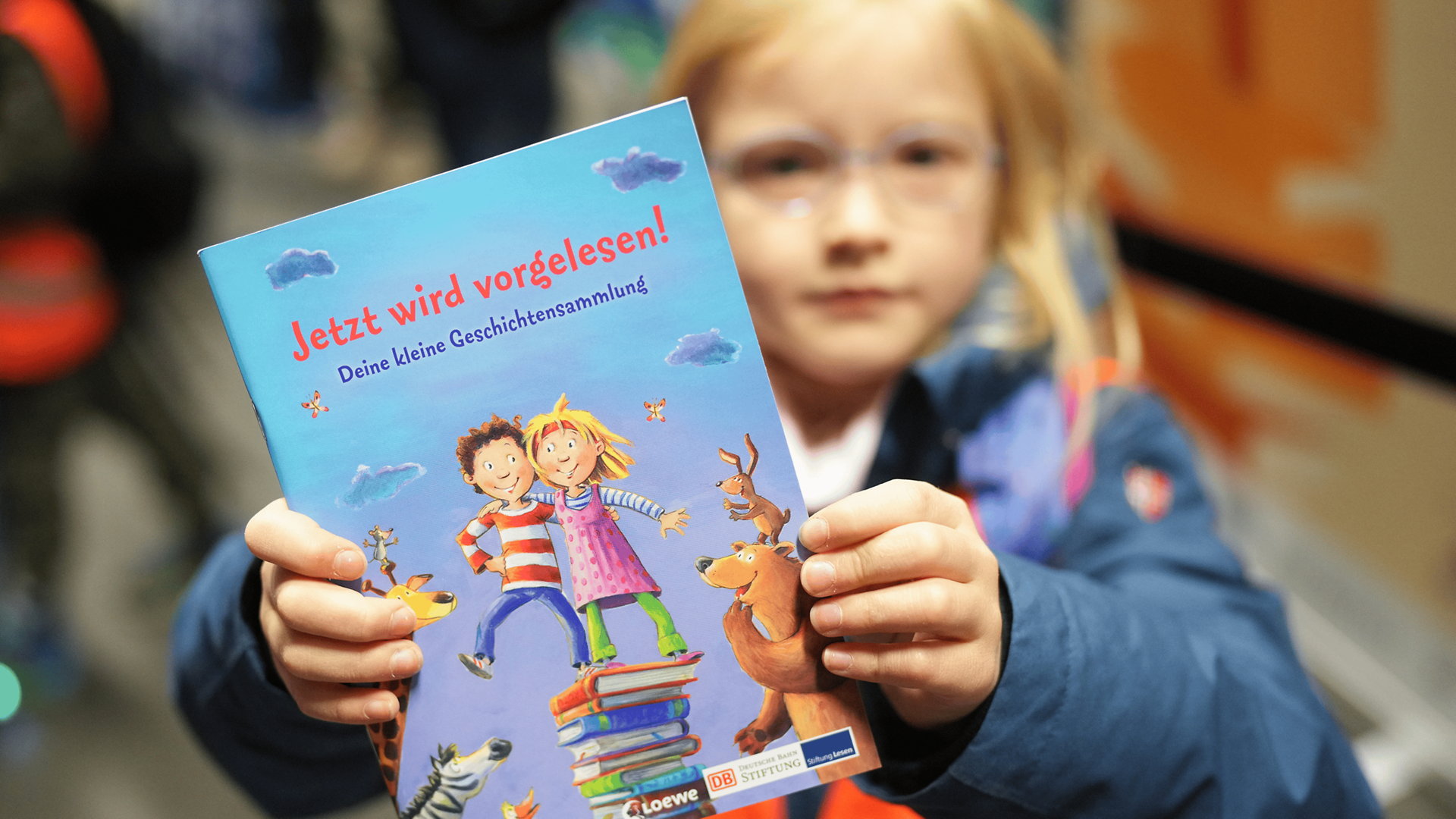 Kleines Mädchen hält Buch "Jetzt wird vorgelesen" hoch