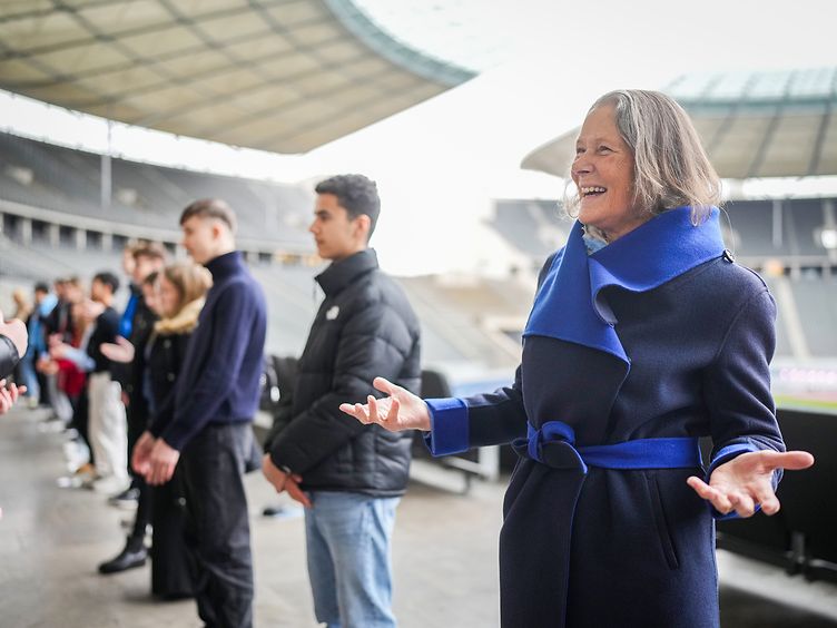 Christina Rau steht im Olympiastadion in Berlin. Im Hintergrund sind weitere Menschen sichtbar